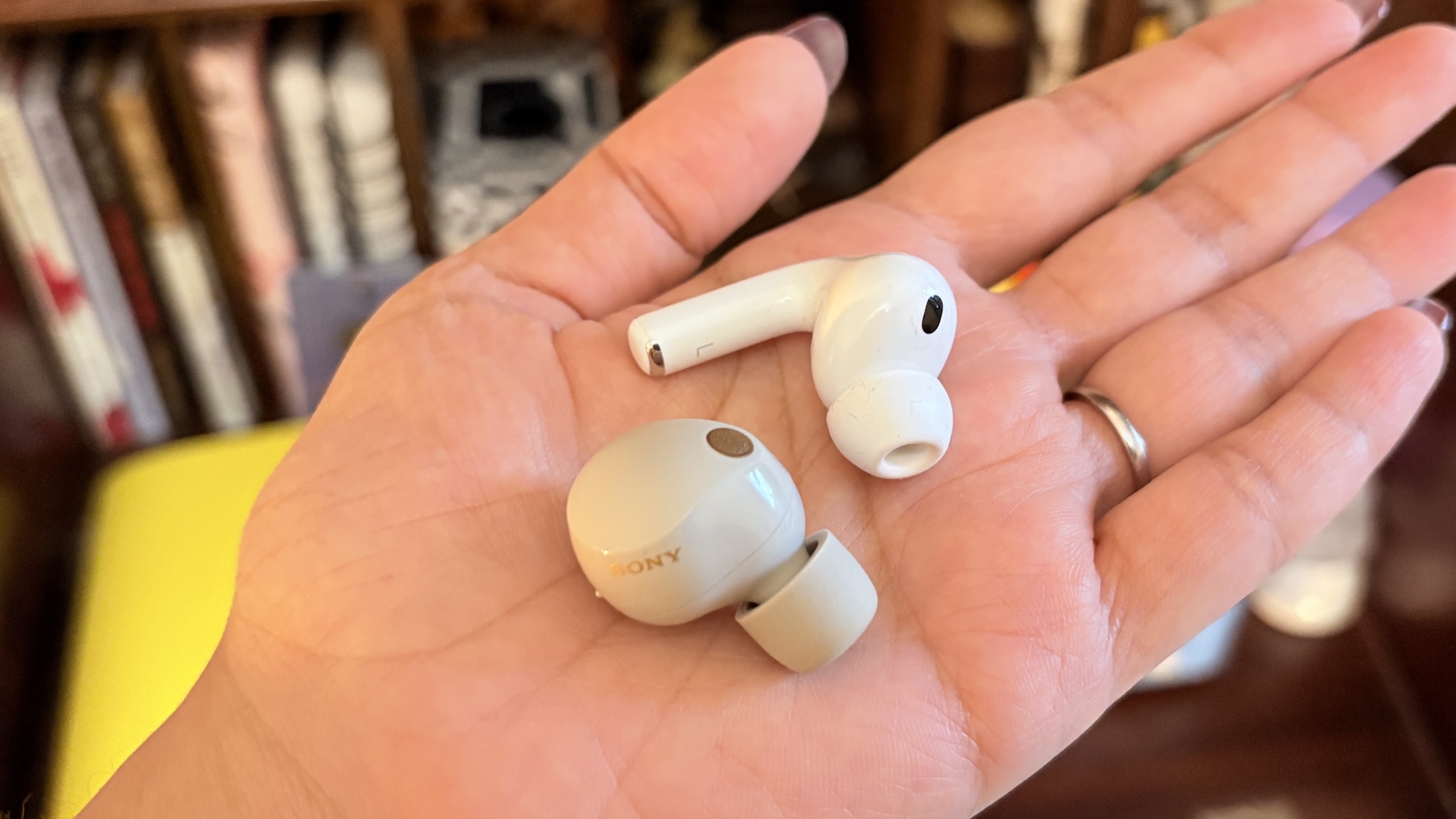 A white AirPods Pro 3 earbud and grey Sony WF-1000XM5 earbud held in the palm of a hand.
