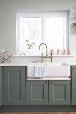 Kitchen sink with green cupboards and a brass tap