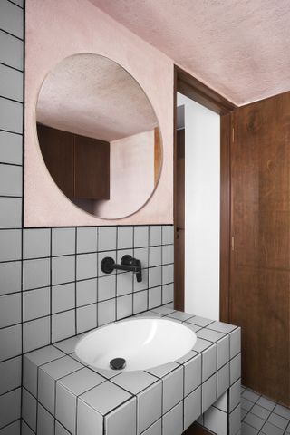 A small bathroom with grey tiles and pink mirror