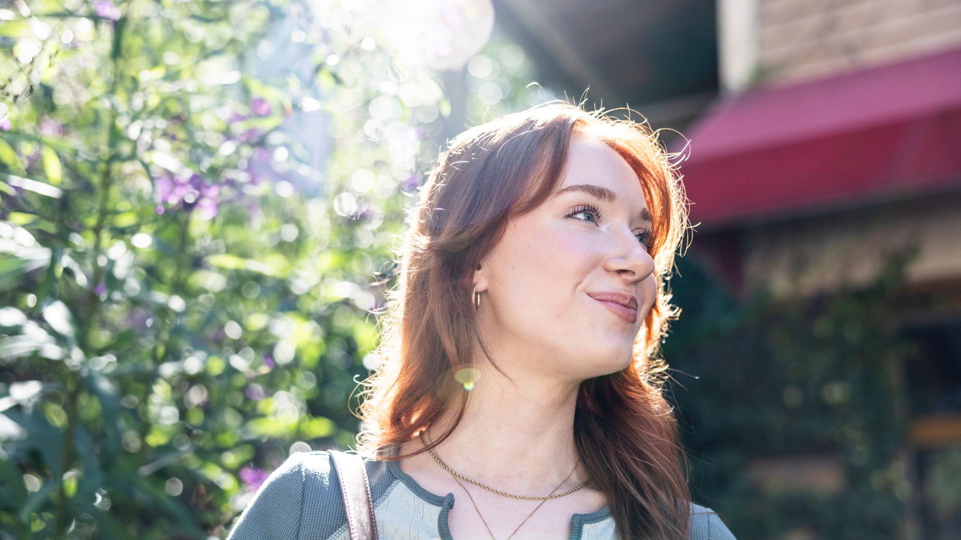 A young woman stands outside in the sunshine smiling.