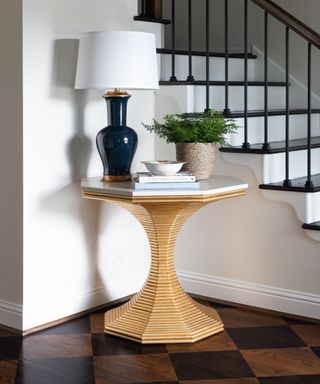 Small entryway table with checkerboard hardwood floor and a vignette styled area with lamp books and a plant