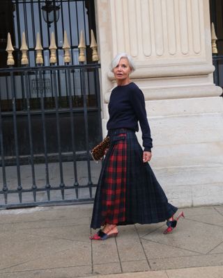 Grece wearing a midi skirt, red sweater, and heels.