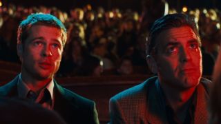 Brad Pitt and George Clooney sitting in a crowd of people looking up.