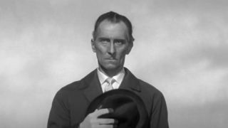 Peter Cushing frowning and holding a hat to his chest in The Man Who Finally Died