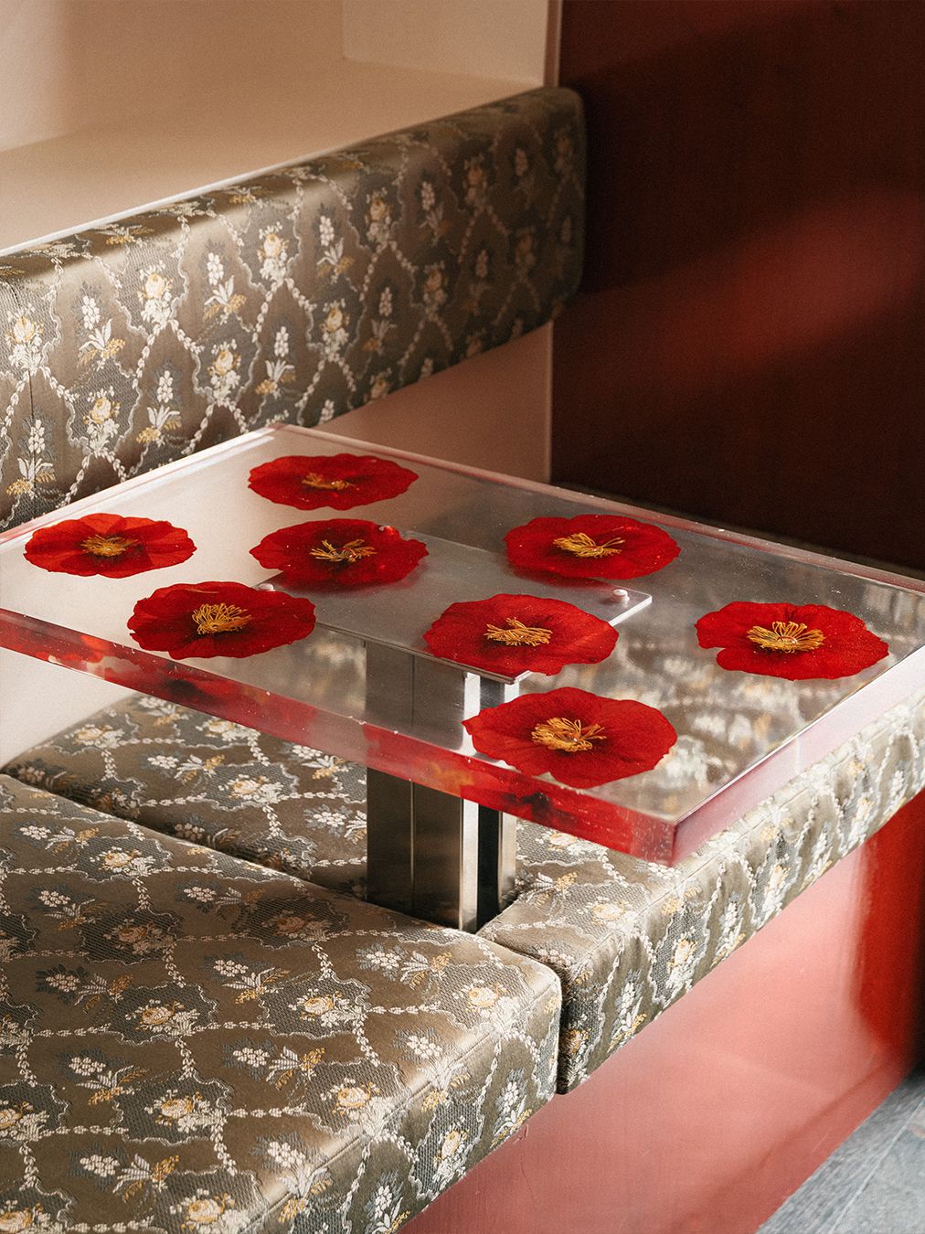 A red-painted wood and chrome bar of a restaurant, decorated with tall, geometrically cut wooden stools with flower-decorated resin backs.