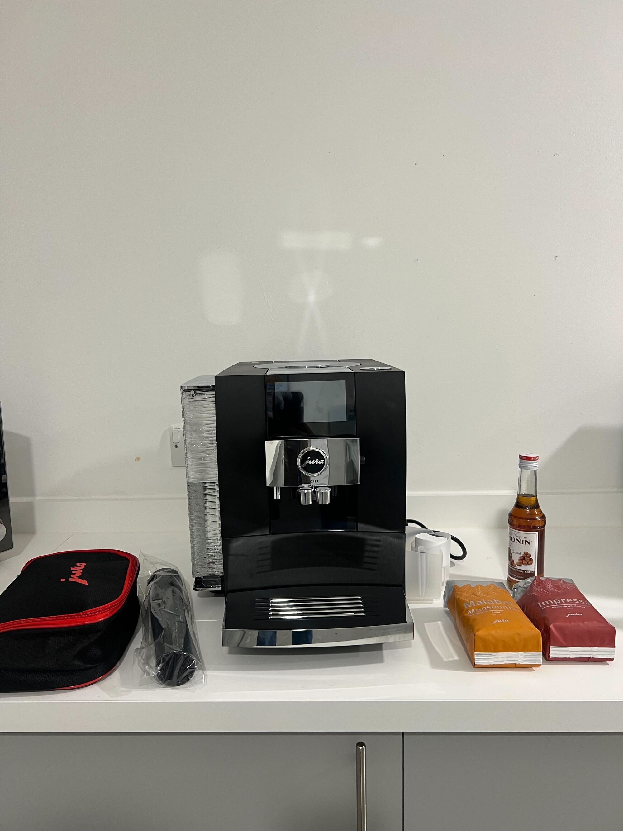 Image of a black Jura Z10 coffee machine sitting on a white kitchen countertop with coffee beans and other coffee accessories around it.