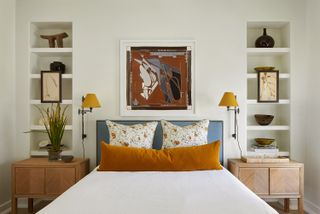 symmetrical bedroom using balance in interior design with orange bolster pillow and wall lights