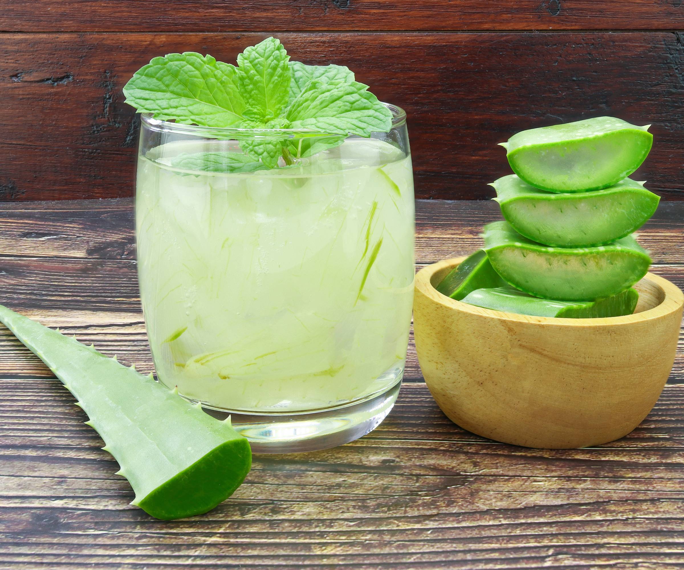 Slices of aloe in a bowl next to a glass of juice with a mint sprig