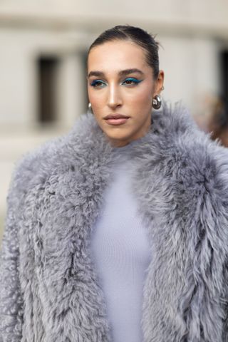 Ginevra Mavilla is seen wearing silver earrings, blue eyeshadow, a long grey long sleeves fur coat and a grey jumpsuit outside the Ferragamo show during the Milan Fashion Week - Womenswear Spring/Summer 2024 on September 23, 2023 in Milan, Italy.
