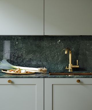 Dark green marble kitchen counter with matching seamless back splash, plus gold faucet and sage green matte cabinetry