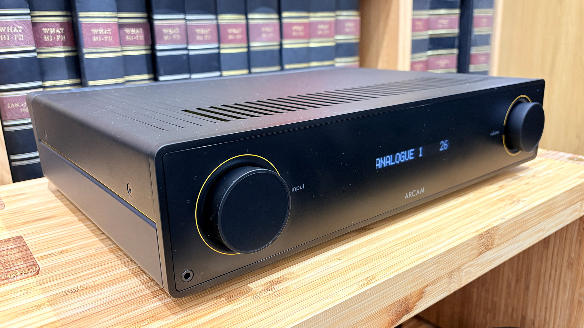 Arcam A15+ integrated amplifier on wooden AV rack in front of bookcase