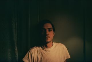 View of a self-portrait of Eggleston wearing a white t-shirt in a dark room