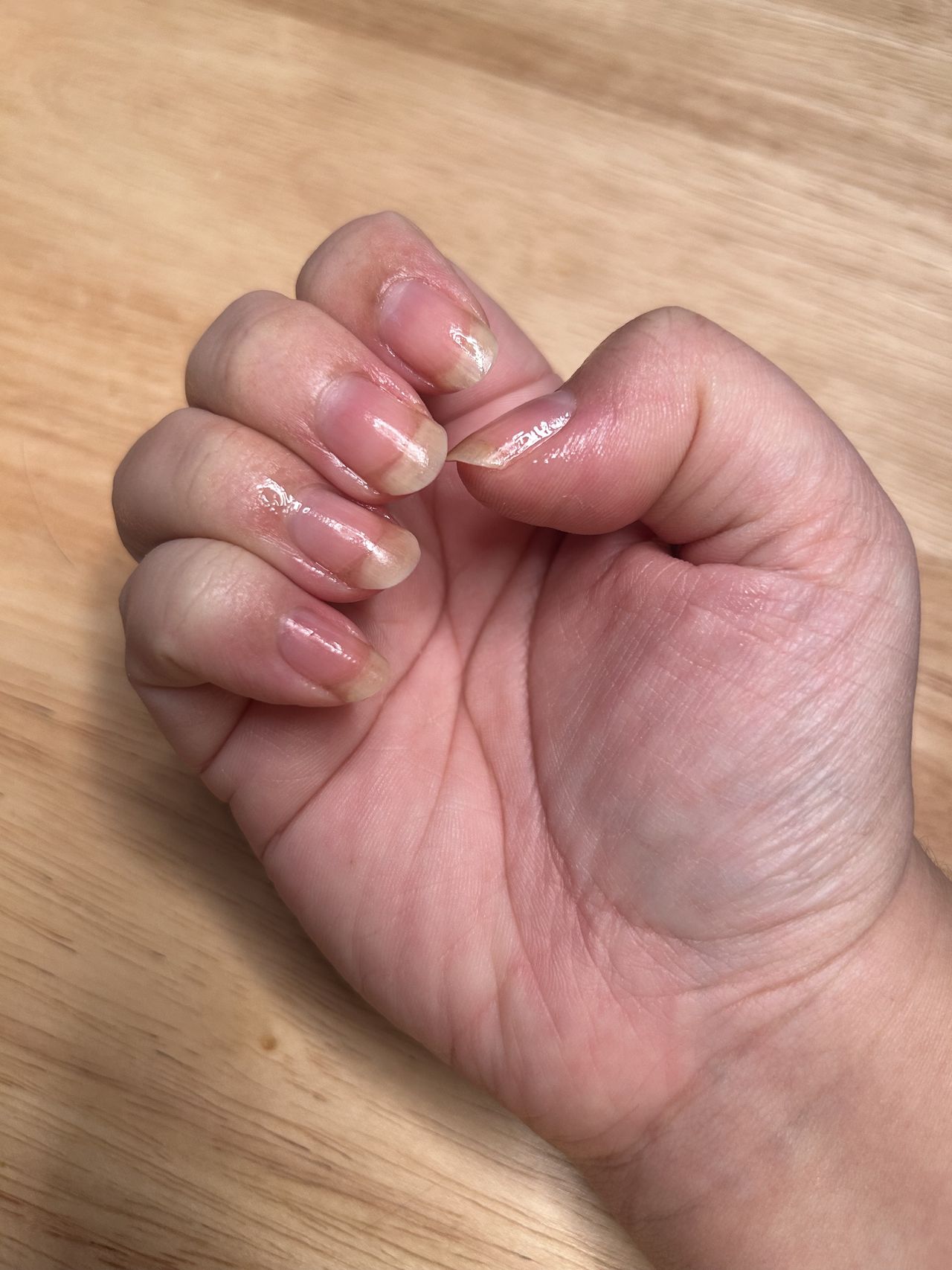 A woman's hand and nails after applying cuticle oil with a wood background and shiny nails.