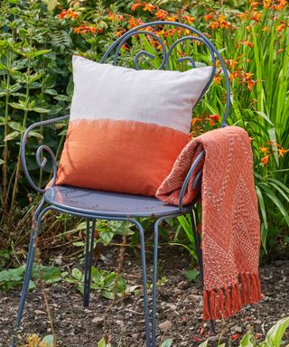garden chair with a terracotta colored cushion and blanket on it