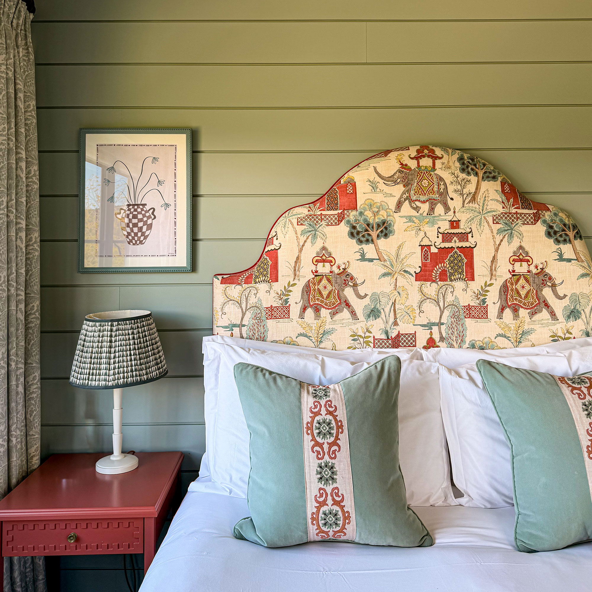 Bed with upholstered patterned headboard and two throw cushions in front of green panelled bedroom walls