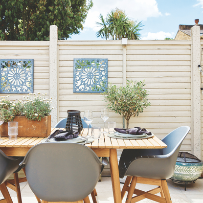 Outdoor dining table and chairs in front of white fence.