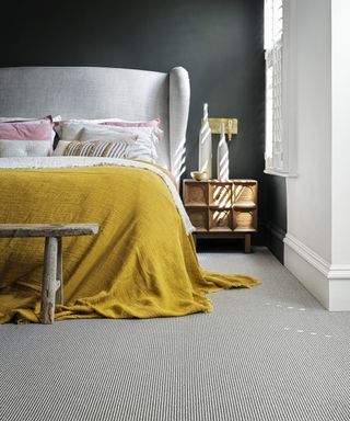 A black bedroom with a pale gray bed and mustard yellow throw