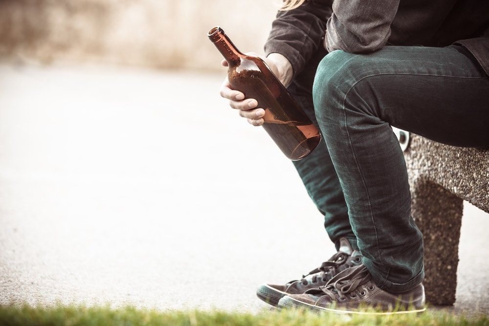 Man depressed with wine bottle sitting on bench outdoor. People abuse and alcoholism problems.