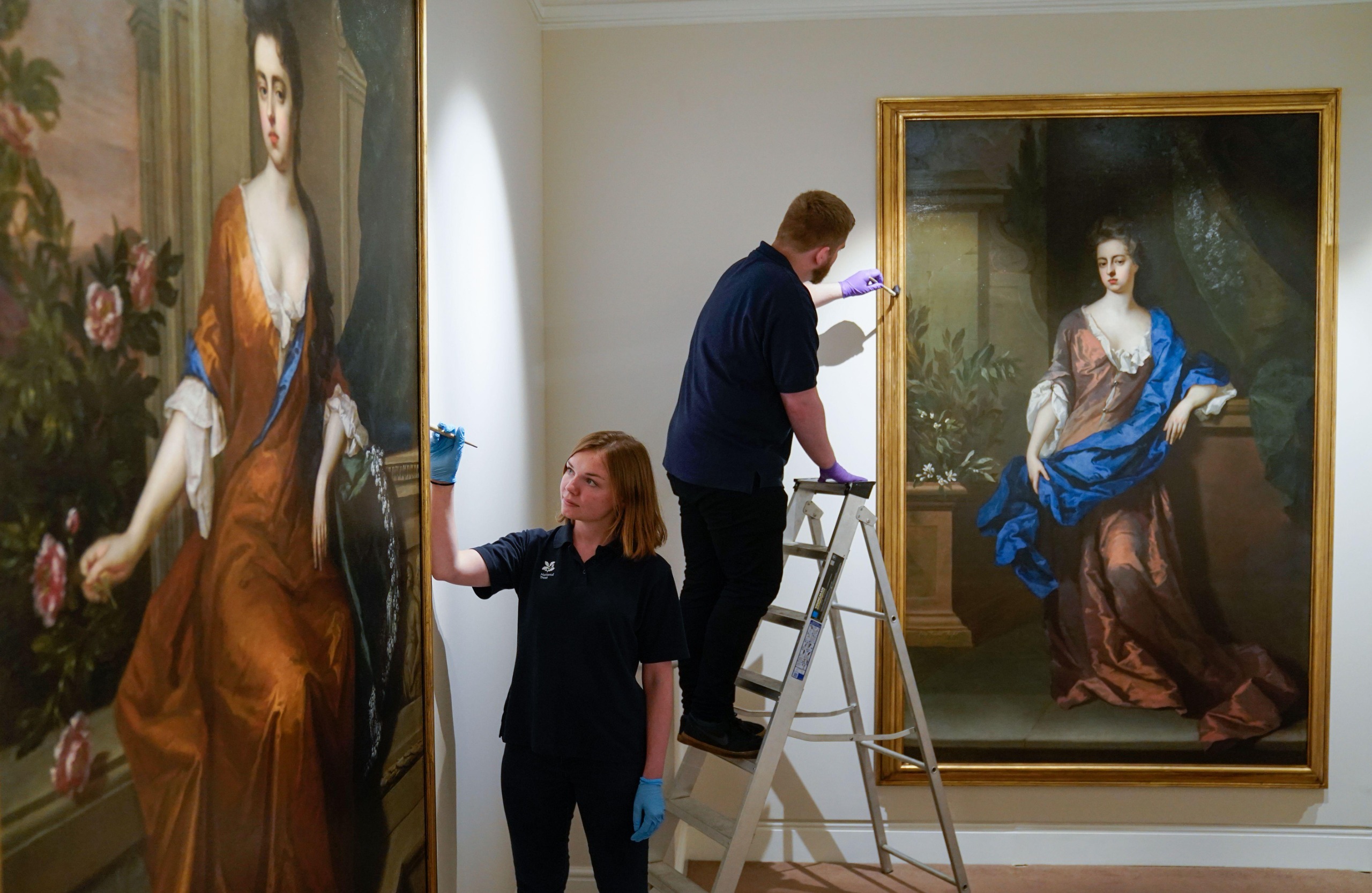 Two conservators apply the finishing touches to two paintings