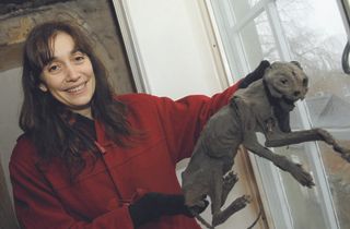 A renovator in a red top holds up a mummified cat found during works to a property