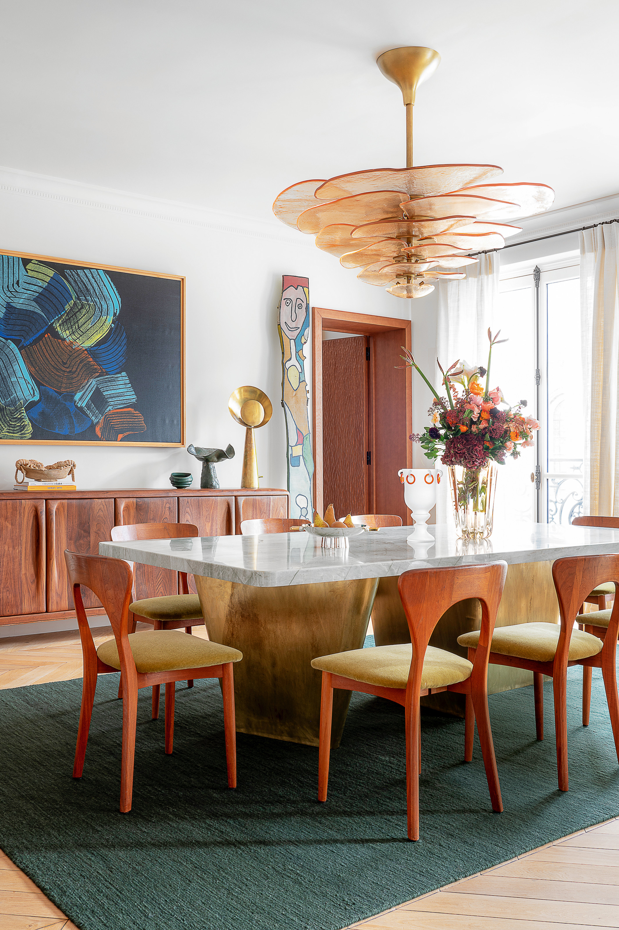 White dining room with gold-base dining table, red wood dining chairs and a glass chandelier