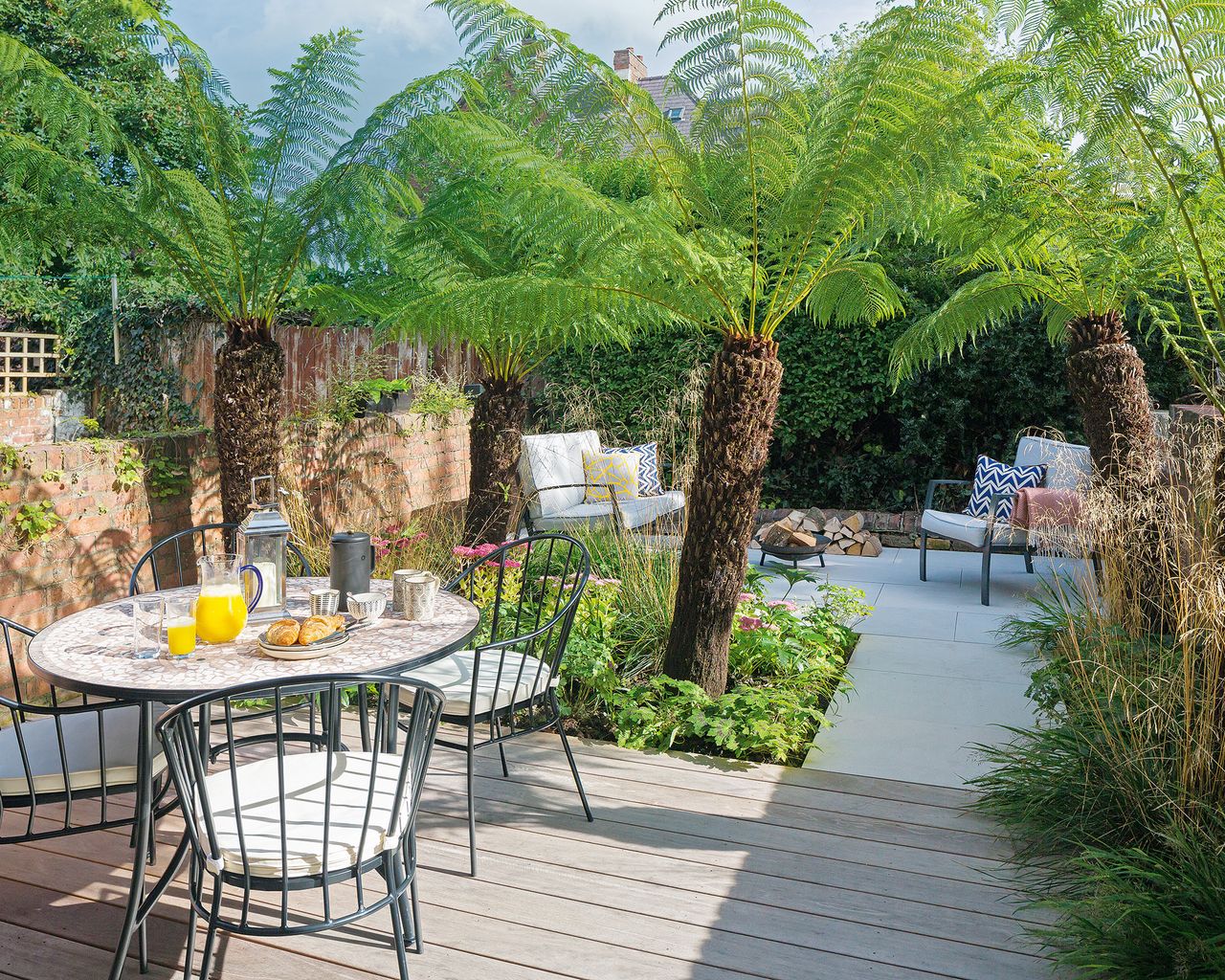 A small garden split into two zoned patio seating areas with tropical style planting