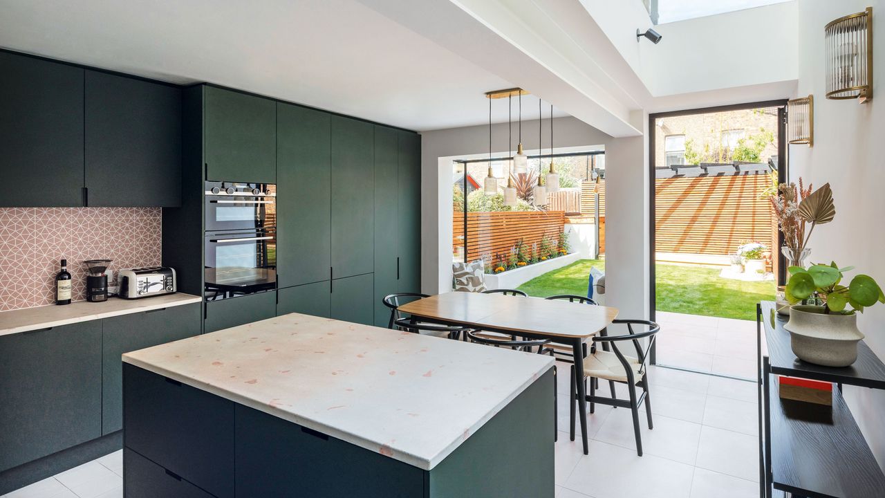 extending into the side return the dark green kitchen with pink splashback and dining table