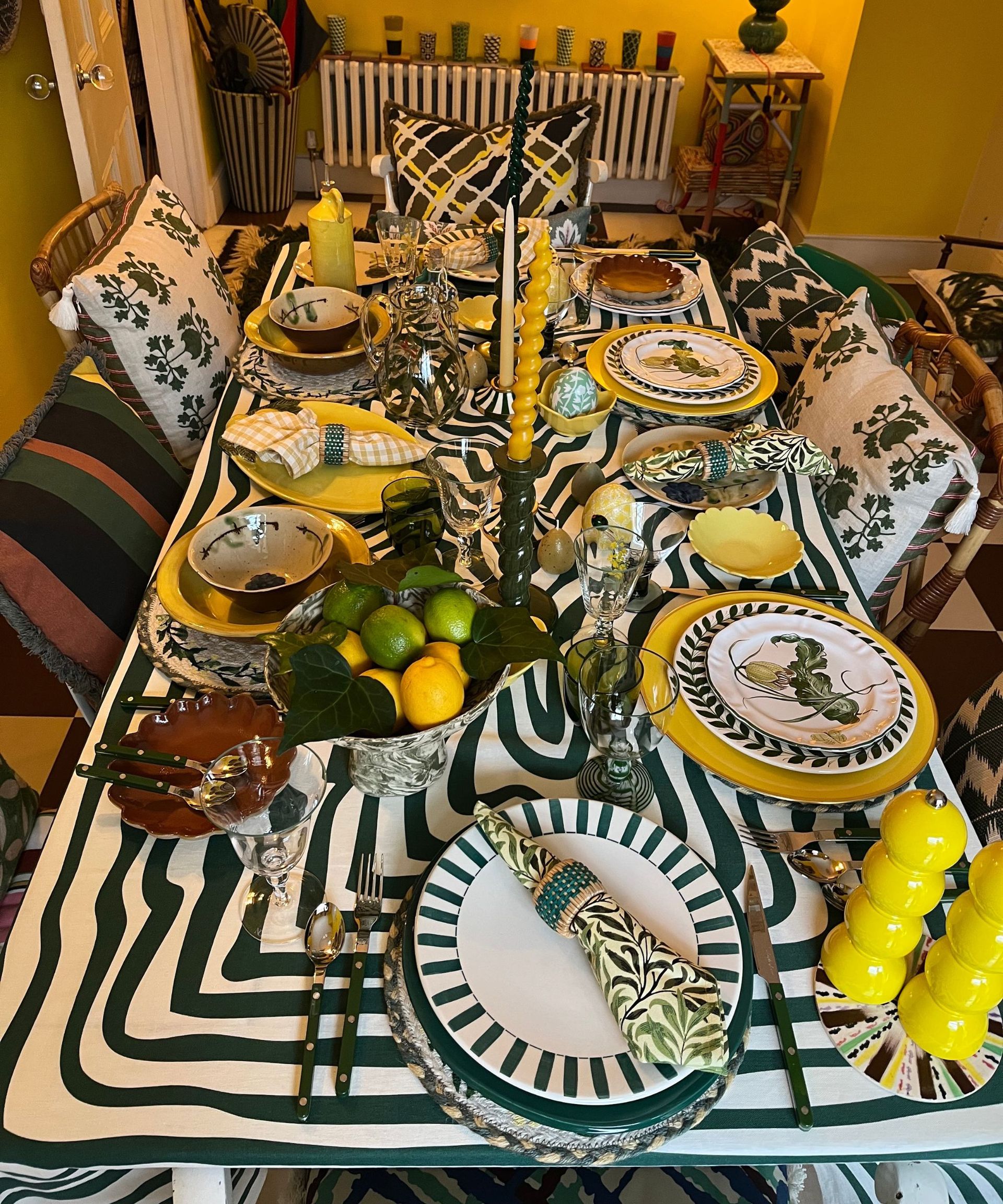Vibrant green and yellow table setting with mis-matched plates, bold tablecloth, bowl of lemons and limes, yellow candles and yellow salt and pepper mills