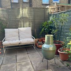 Green chiminea in a patio courtyard garden with a striped sofa