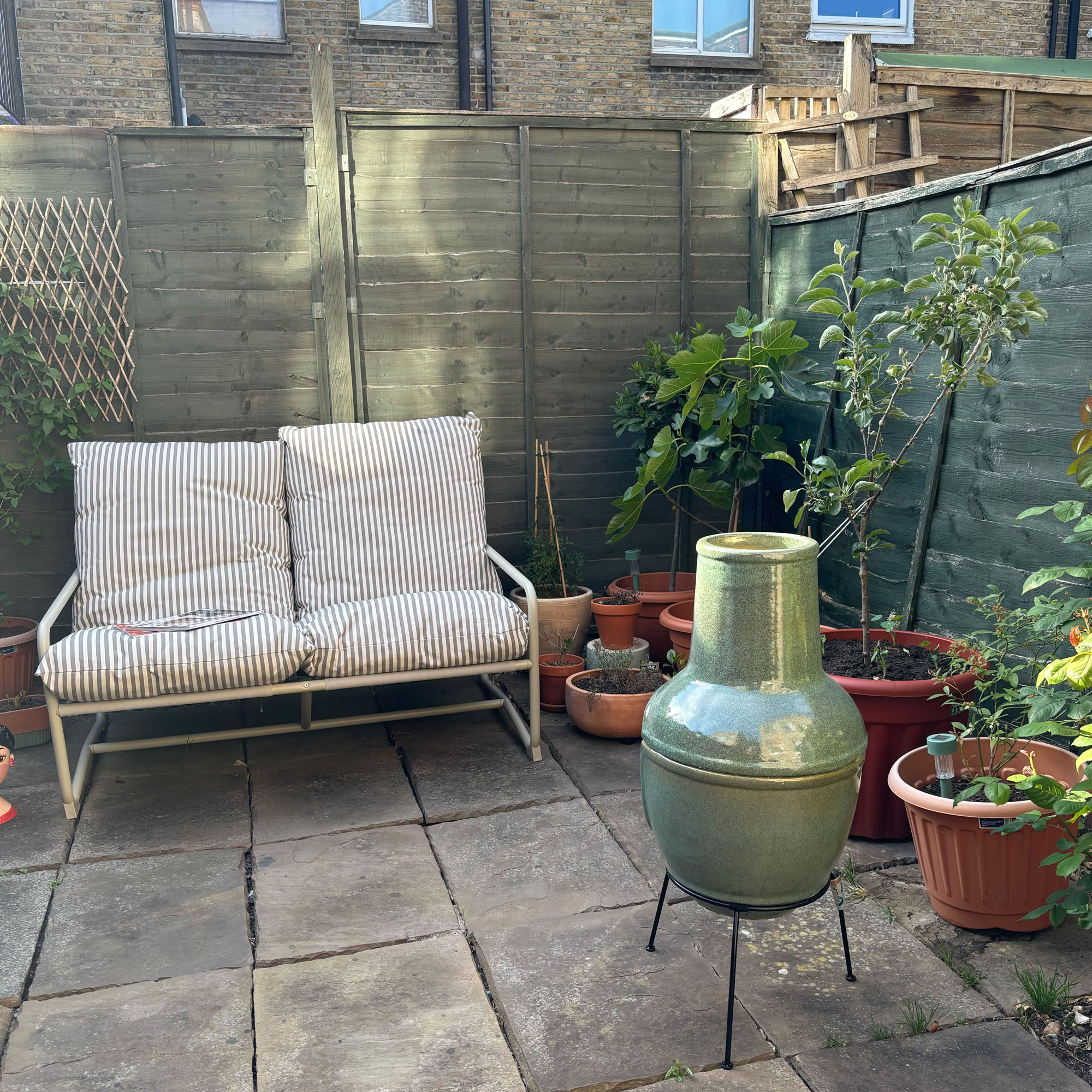 Green chiminea in a patio courtyard garden with a striped sofa
