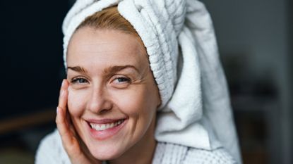 Best moisturiser for mature skin - woman with towel on head applying face cream while smiling