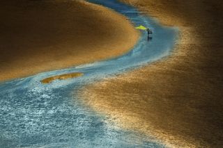 A beach reflects the golden haze of the sunset, while a traditional fisherman wades through the water in China