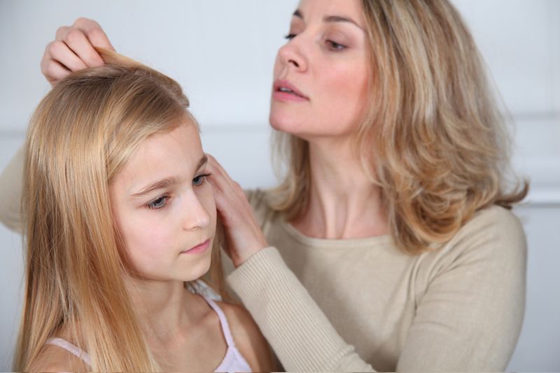 A mom fine-tooth combs her daughter&#039;s hair.