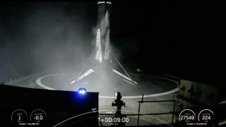 the first stage of a spacex falcon 9 rocket rests on the deck of a drone ship at sea at night.