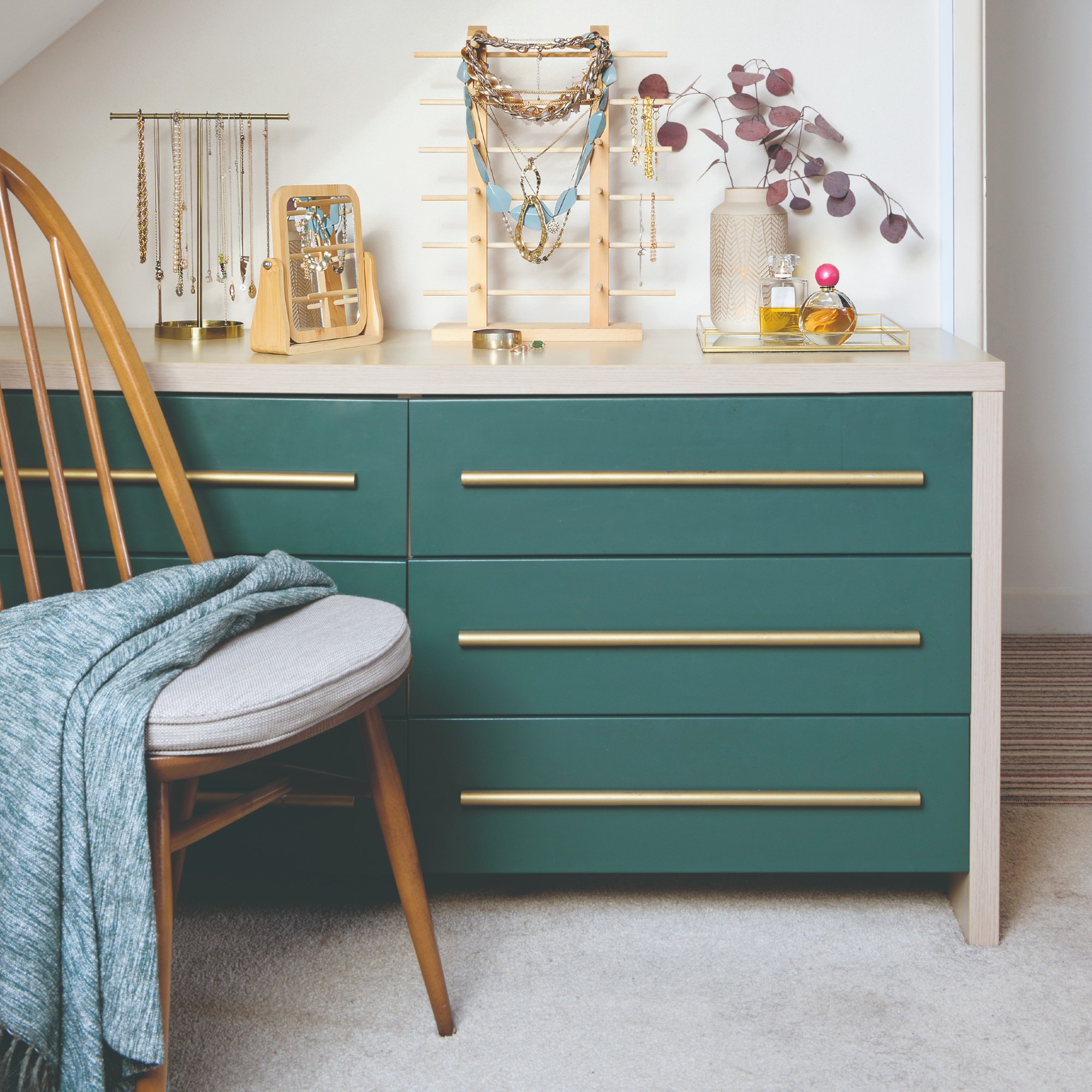 A bedroom with green chest of drawers with a retro chair and a jewellery display