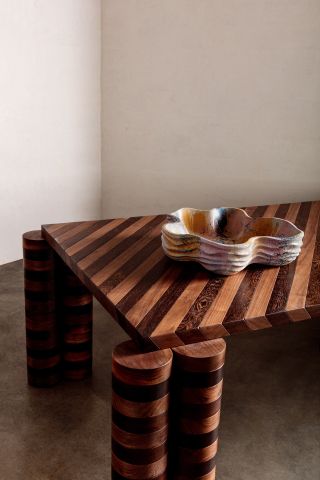 Striped dining table with 2 cylinder shaped legs one each corner with a hand-molded colourful bowl