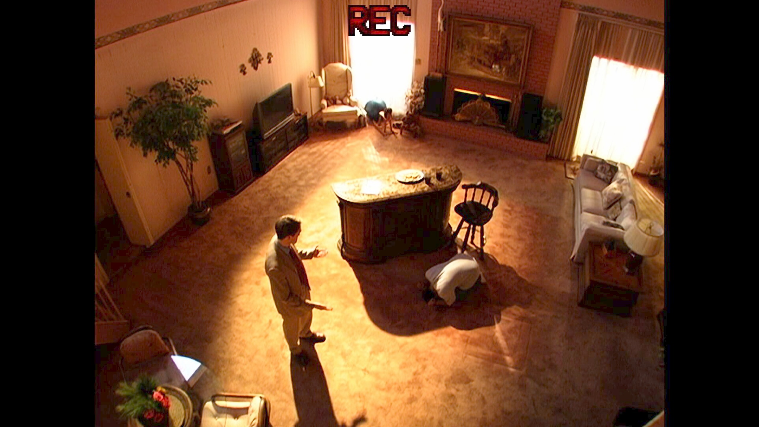 A birds-eye view of one man in a suit (Robert Pattinson as Chris Hansen standing in a living room as another man in a white shirt bows in front of him, in A24's 'Primetime.'