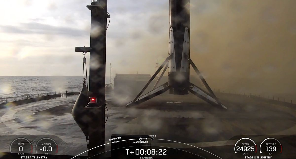 A black and white spacex falcon 9 rocket first stage sits on the deck of a ship at sea.