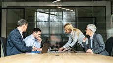 A divorcing couple sit across from each other with their divorce attorneys at a conference table.