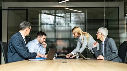 A divorcing couple sit across from each other with their divorce attorneys at a conference table.