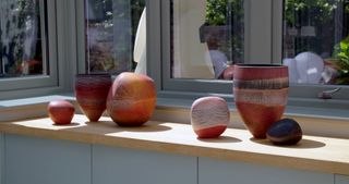 Colourful ceramics in different sizes, colours and forms, displayed on a shelf top next to a window