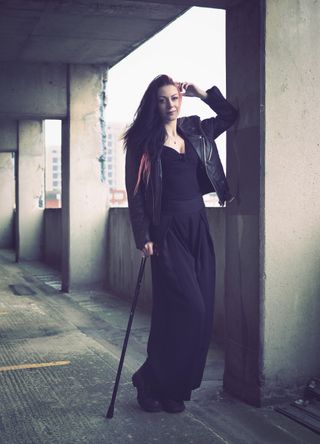 Portrait of a person with a cane standing in an industrial setting, taken on the OM System OM-3 with the OM System 25mm f/1.8 II lens