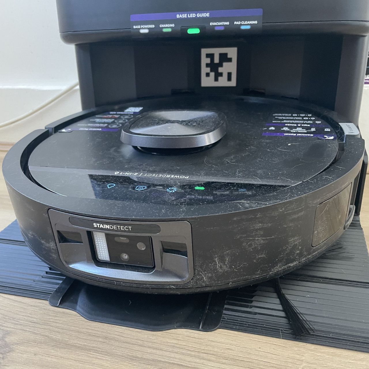 Shark PowerDetect UV robot vacuum sitting on its base, covered in dust and hair
