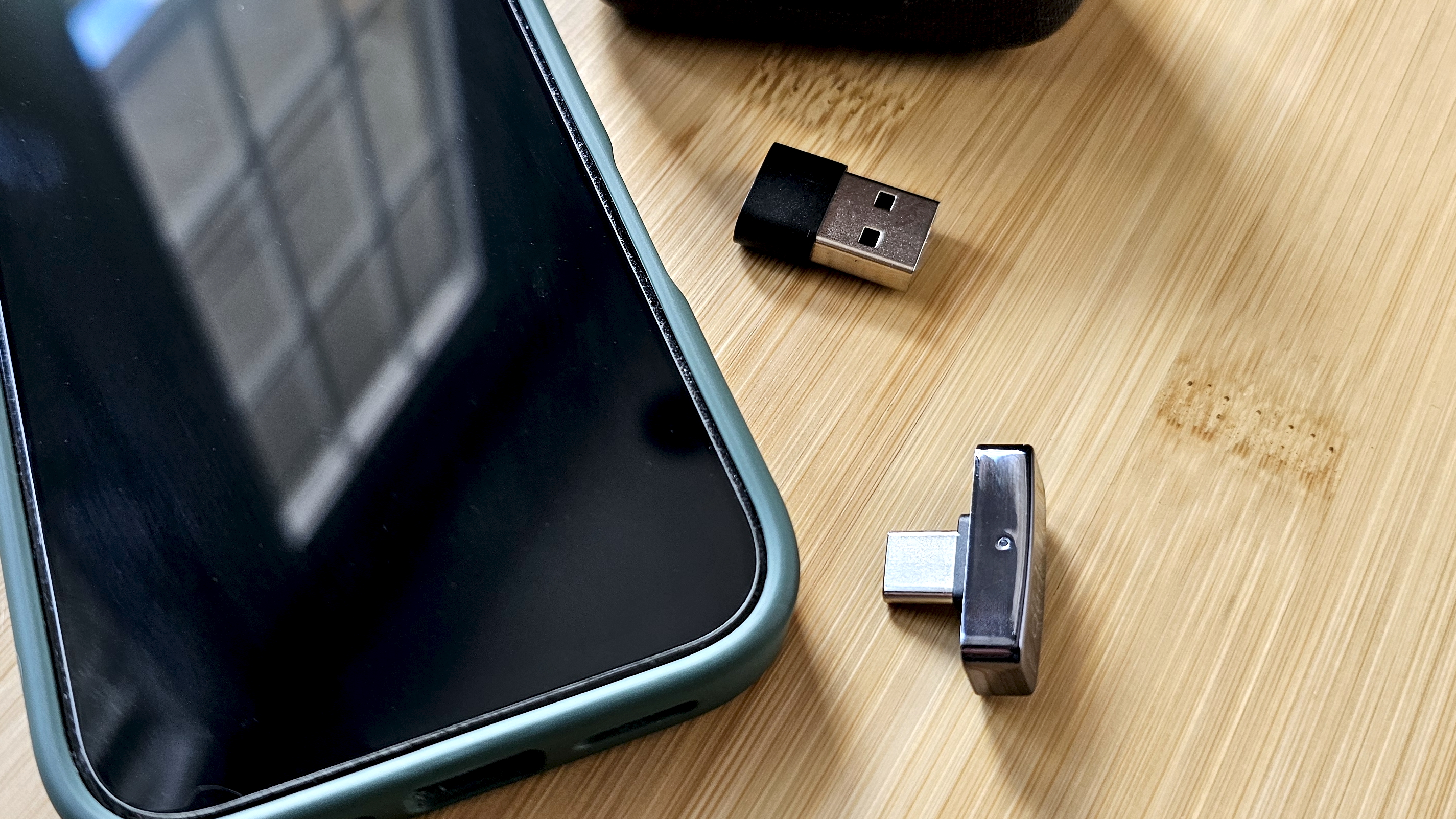 The Questyle QCC Dongle Pro with a smartphone to denote size, on a light wooden table