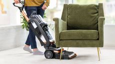 Person using the Bissell Revolution HydroSteam on carpet under a green armchair