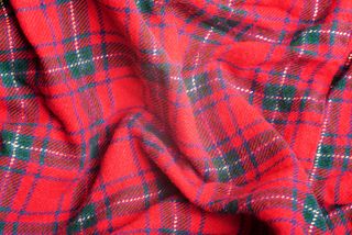 A close up of a red, knitted tartan plaid design blanket.