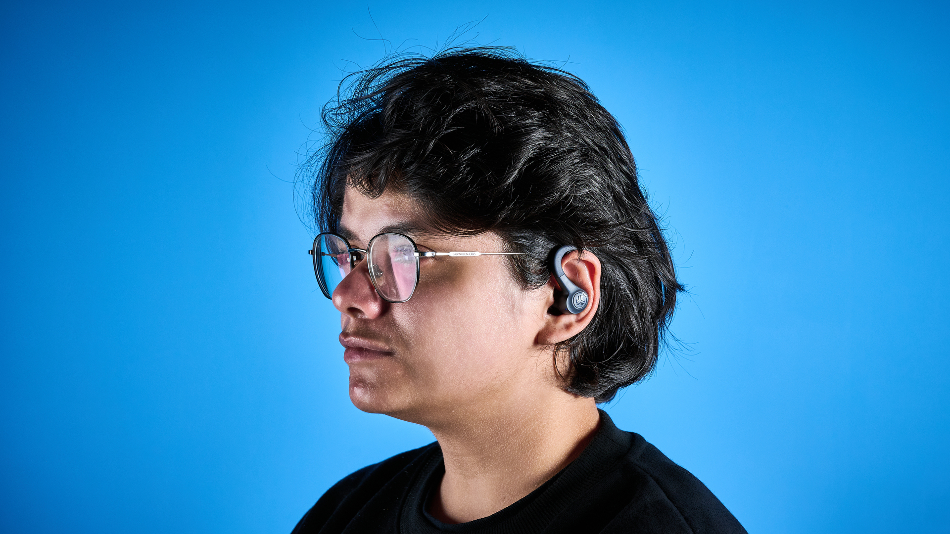 the jlab go sport+ earbuds photographed against the blue tom's guide background, showing charging case and wearing style