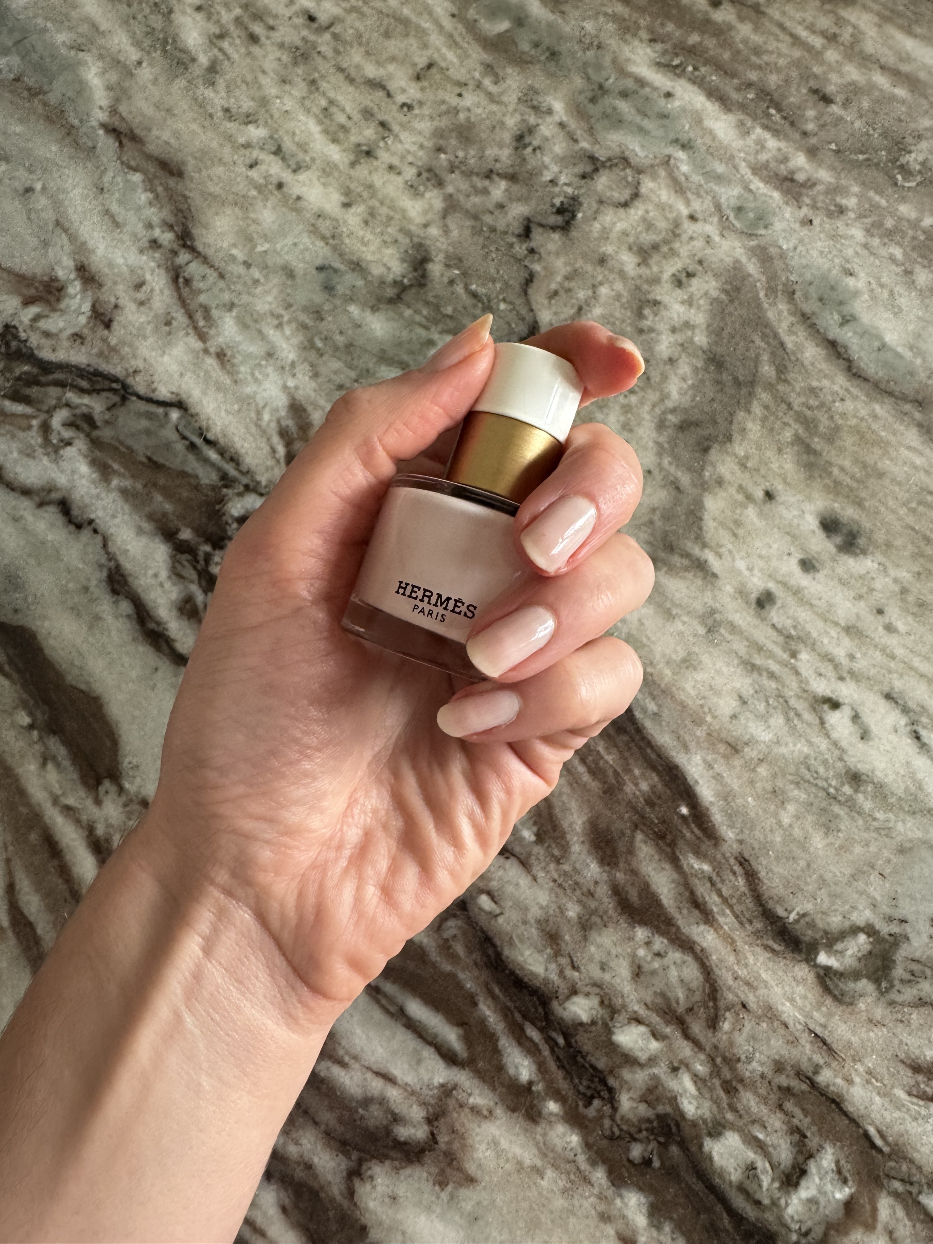 Eleanor holding a bottle of Hermes nail polish in shade Rose Porcelaine and wearing three coats of the polish on her nails