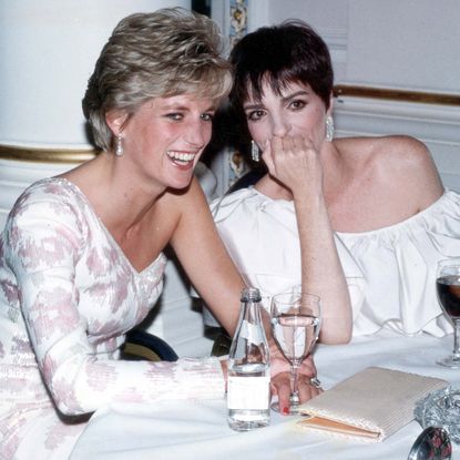 Princess Diana wearing a white gown sitting at a table laughing with Liza Minelli