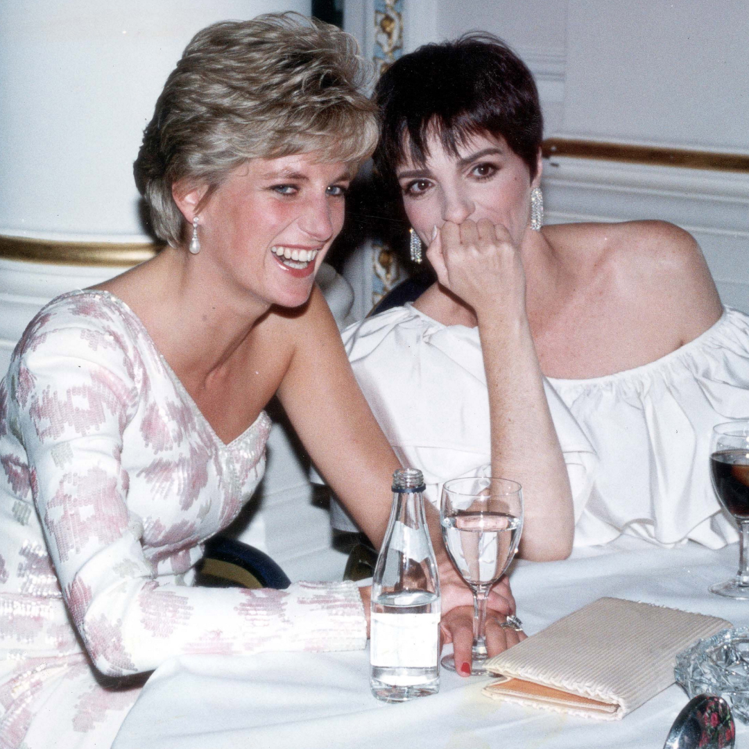 Princess Diana wearing a white gown sitting at a table laughing with Liza Minelli